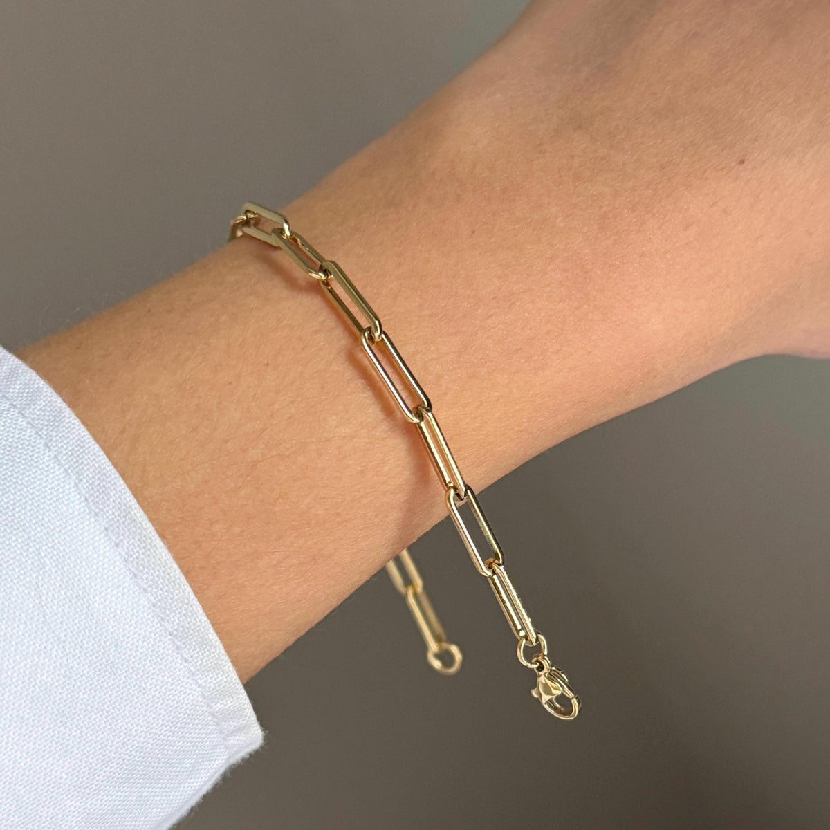 Gold plated paperclip bracelet worn open on wrist showing elongated links and lobster clasp