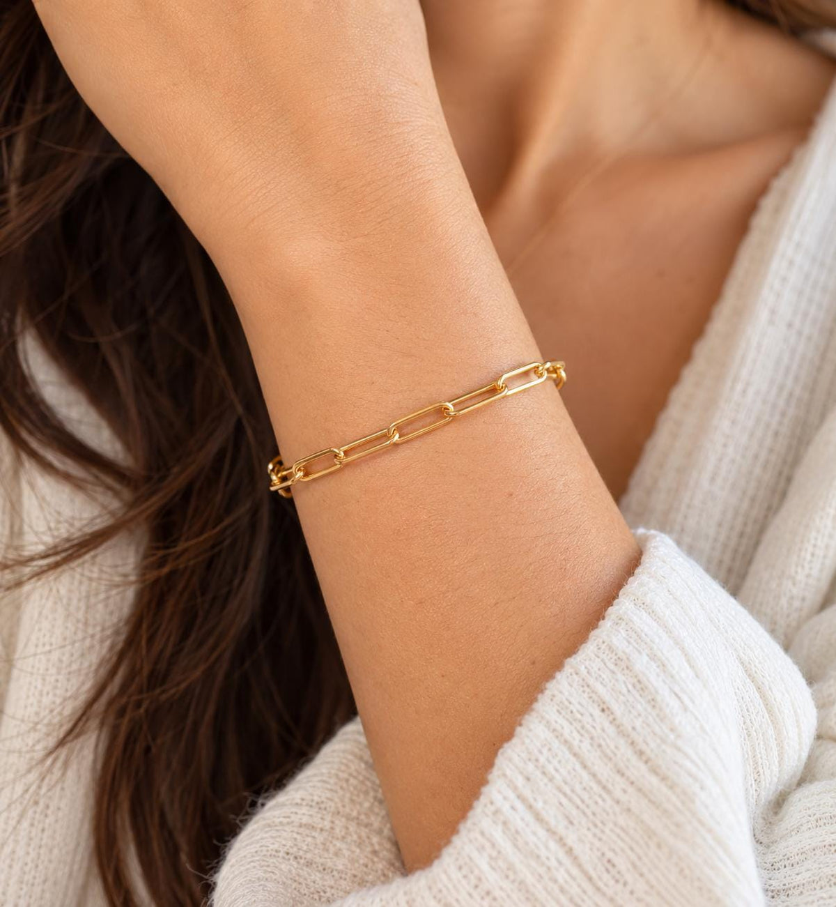 Minimalist gold plated paperclip chain bracelet styled on wrist with cream knit sleeve