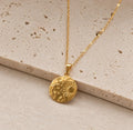 Gold plated celestial medallion necklace with sun moon and star details on beige stone
