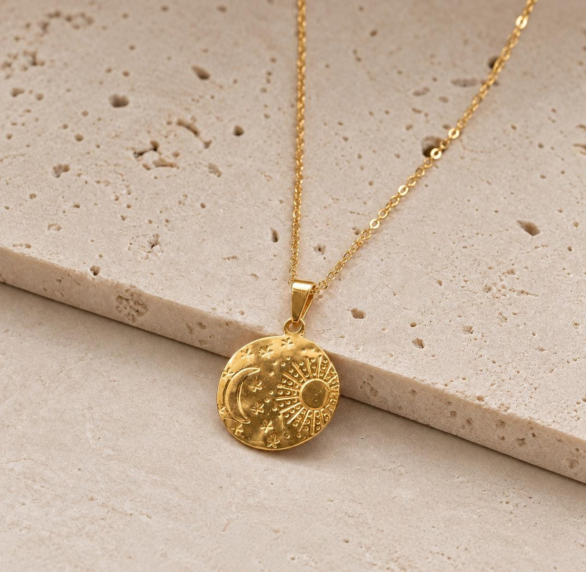 Gold plated celestial medallion necklace with sun moon and star details on beige stone