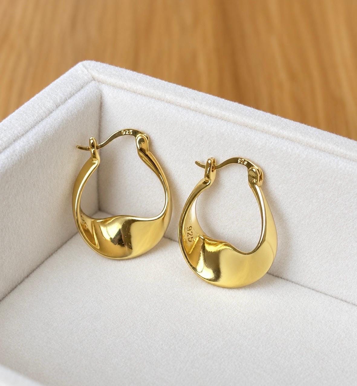 Pair of 18K gold plated 925 sterling silver organic twist hoop earrings displayed on cream velvet