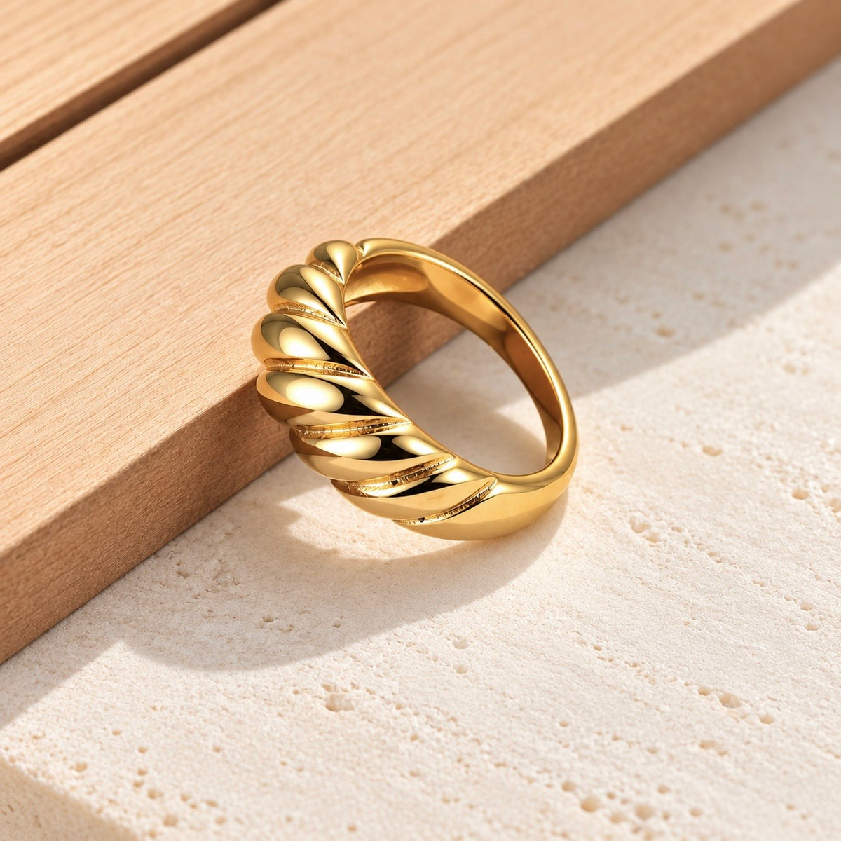 18K gold plated chunky croissant twist ring on pale stone with warm wood backdrop