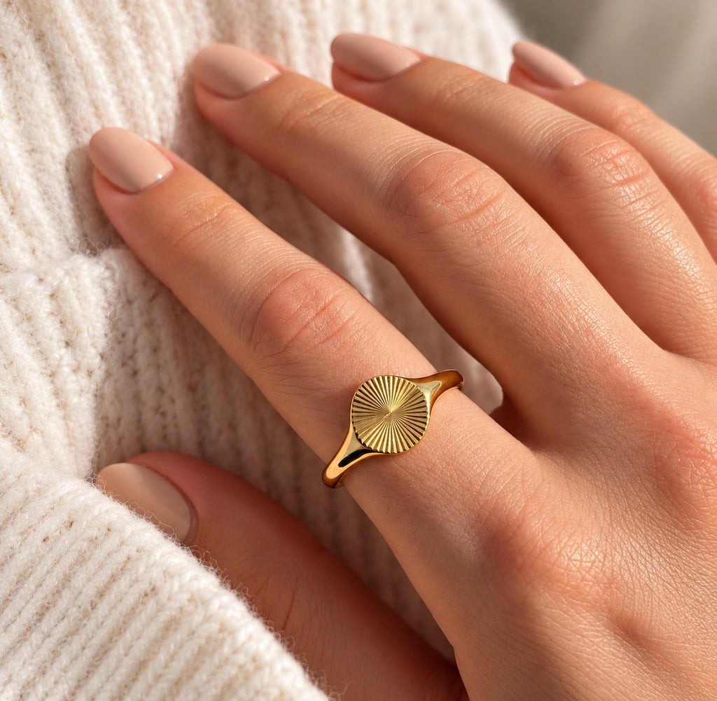 Gold plated sunburst signet ring worn on finger with neutral knitwear