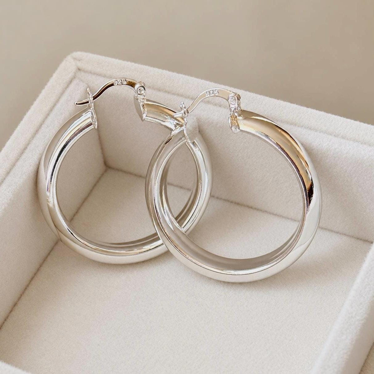 Close-up angled view of 925 sterling silver hoop earrings showing polished tubular profile and 925 stamp
