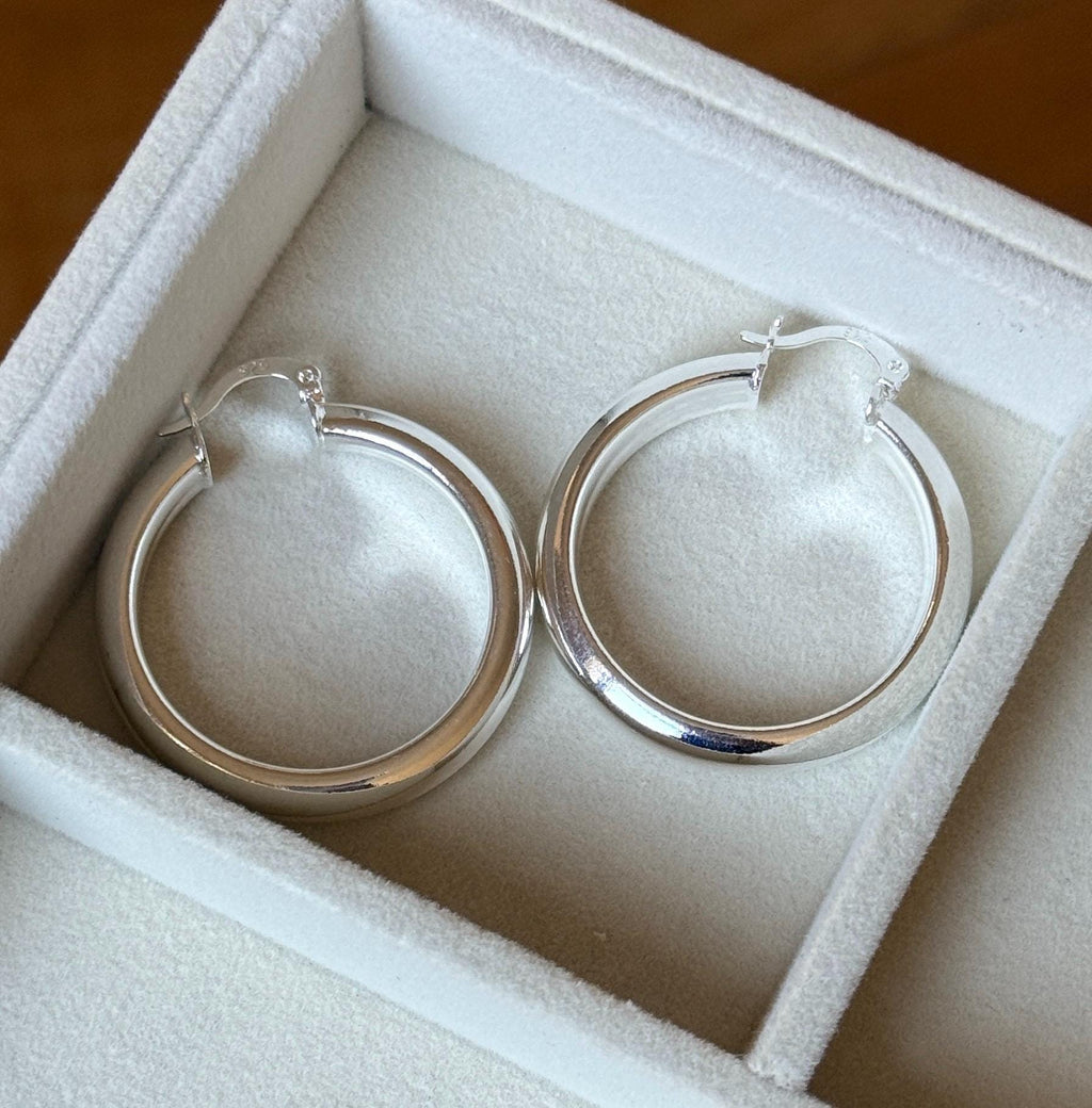 Close view of two 35mm sterling silver round hoop earrings inside velvet tray