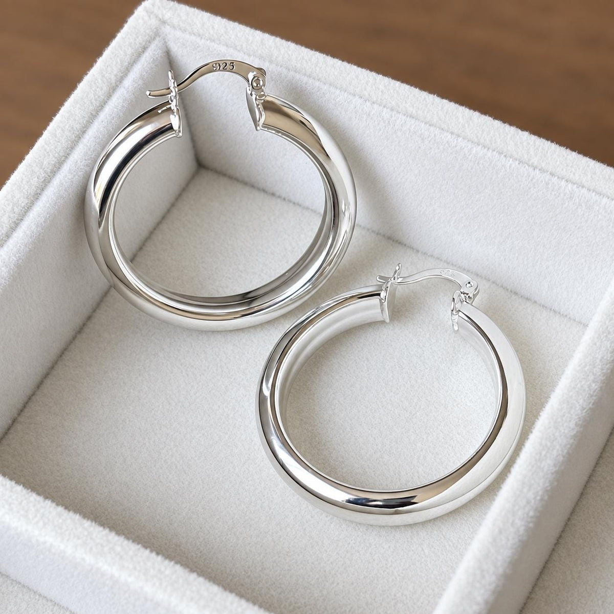 Pair of 35mm polished 925 sterling silver hoop earrings with hinged closures in an ivory velvet jewellery tray