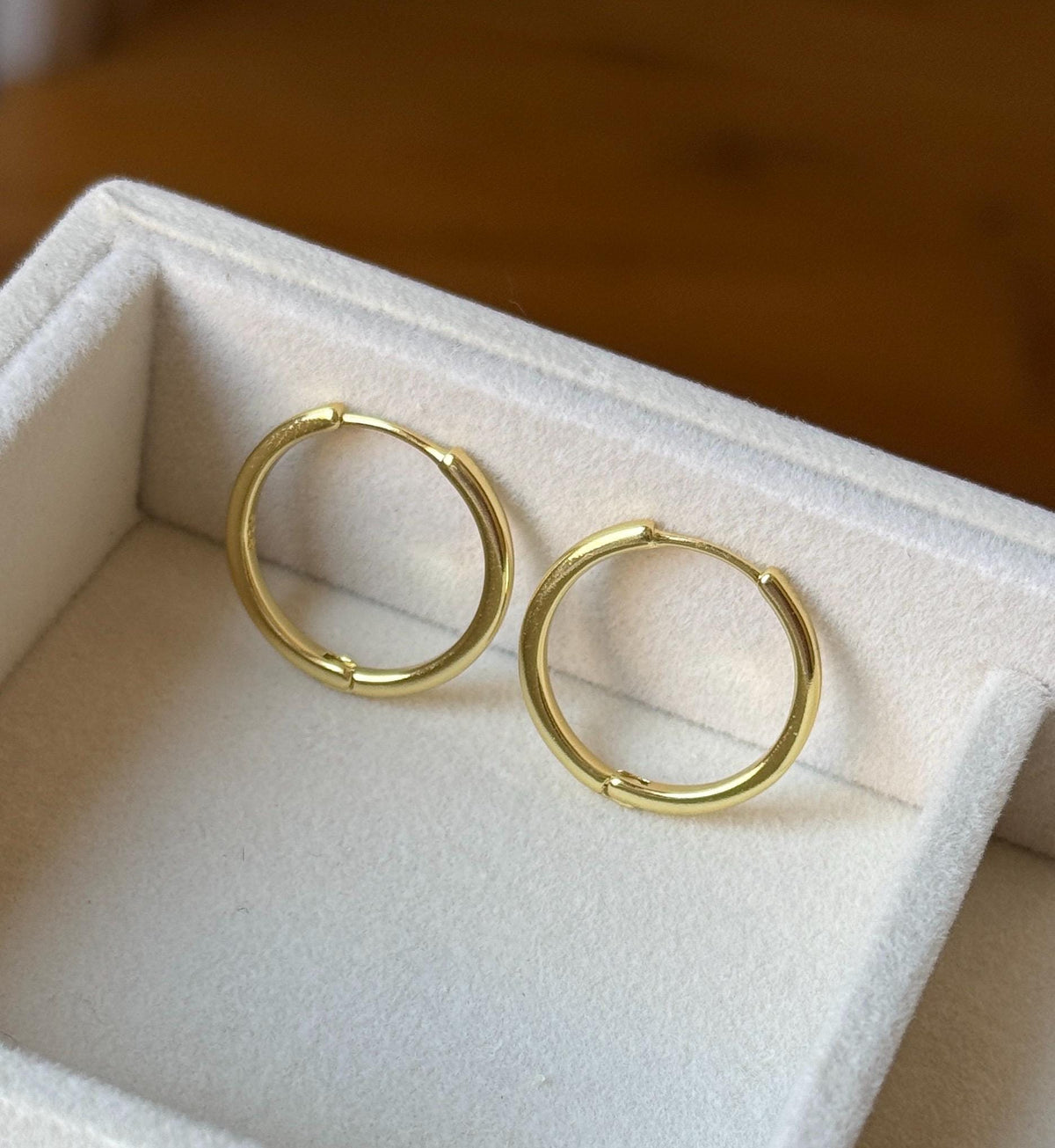 Polished gold plated 925 sterling silver classic hoop earrings displayed on soft ivory jewellery tray