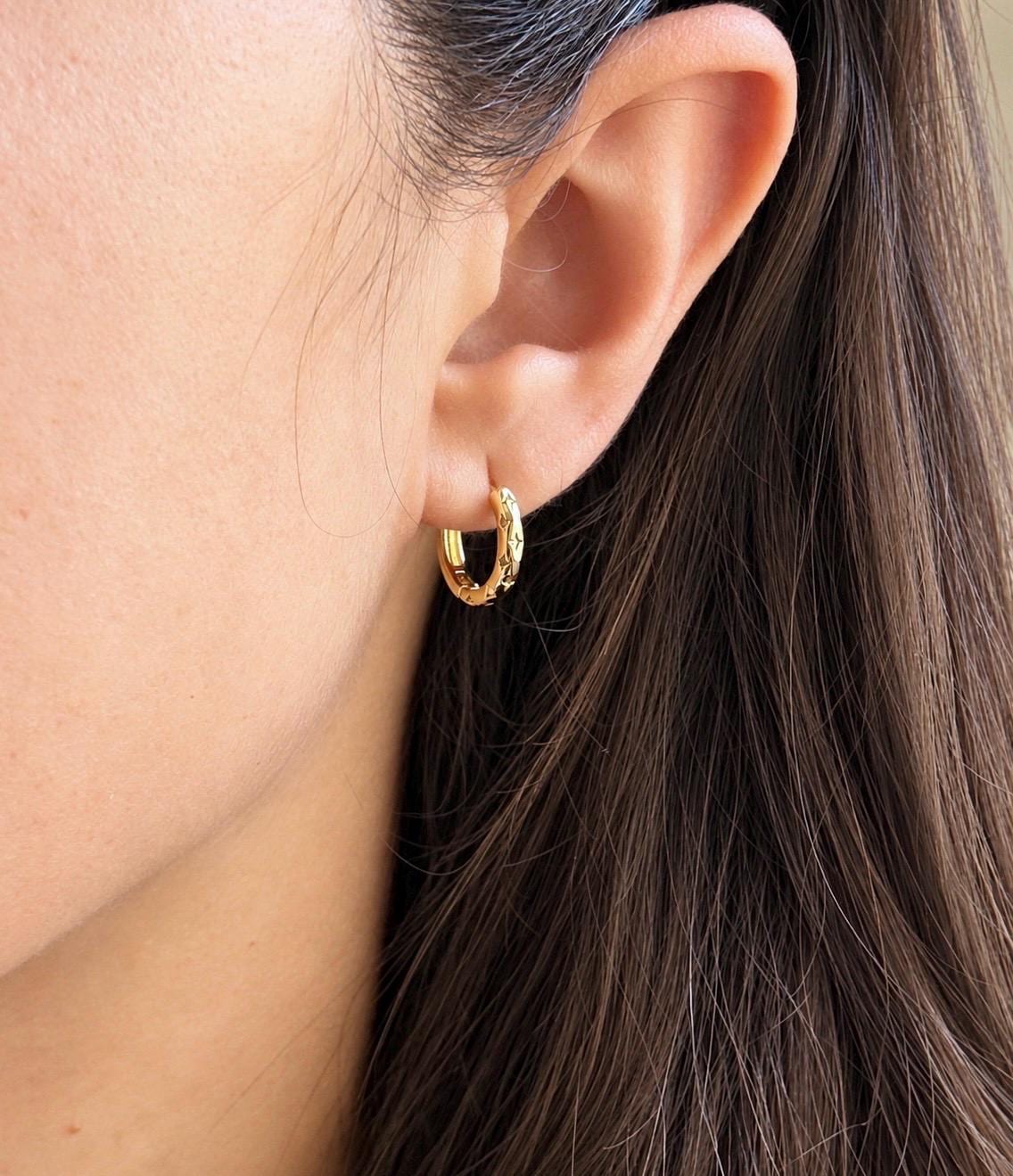Gold plated sterling silver star engraved huggie hoop earring modelled on ear