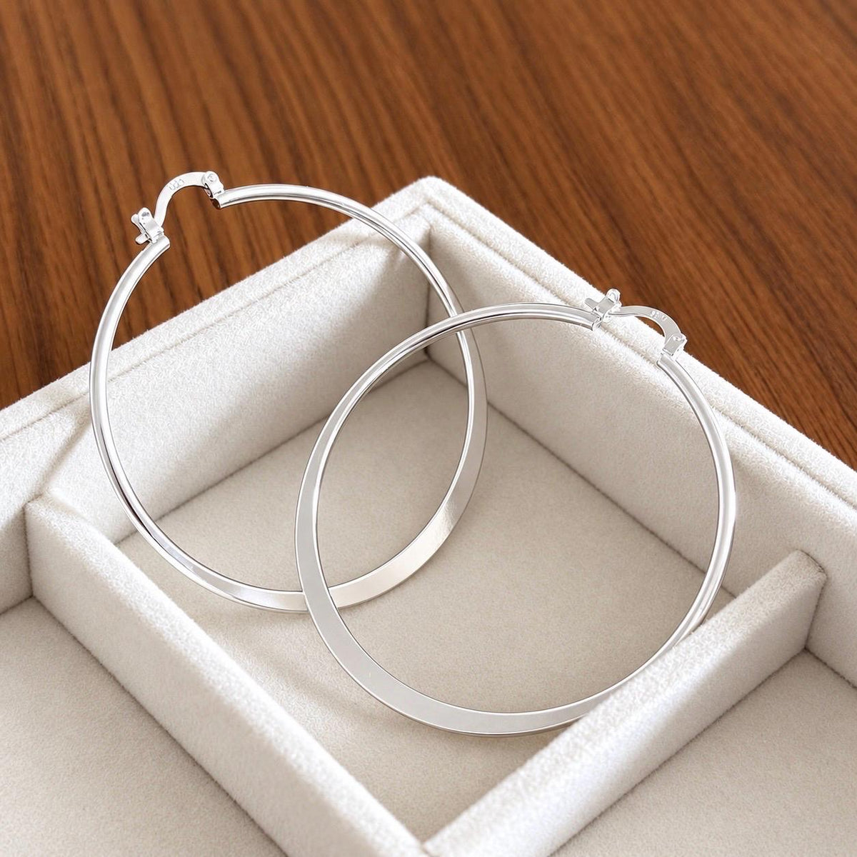 Large round 55mm sterling silver hoop earrings seen at an angle on white jewellery tray