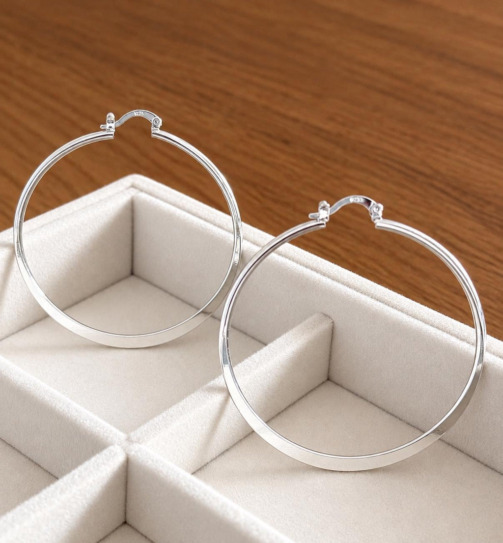 Pair of large 55mm polished 925 sterling silver hoop earrings displayed on cream jewellery tray