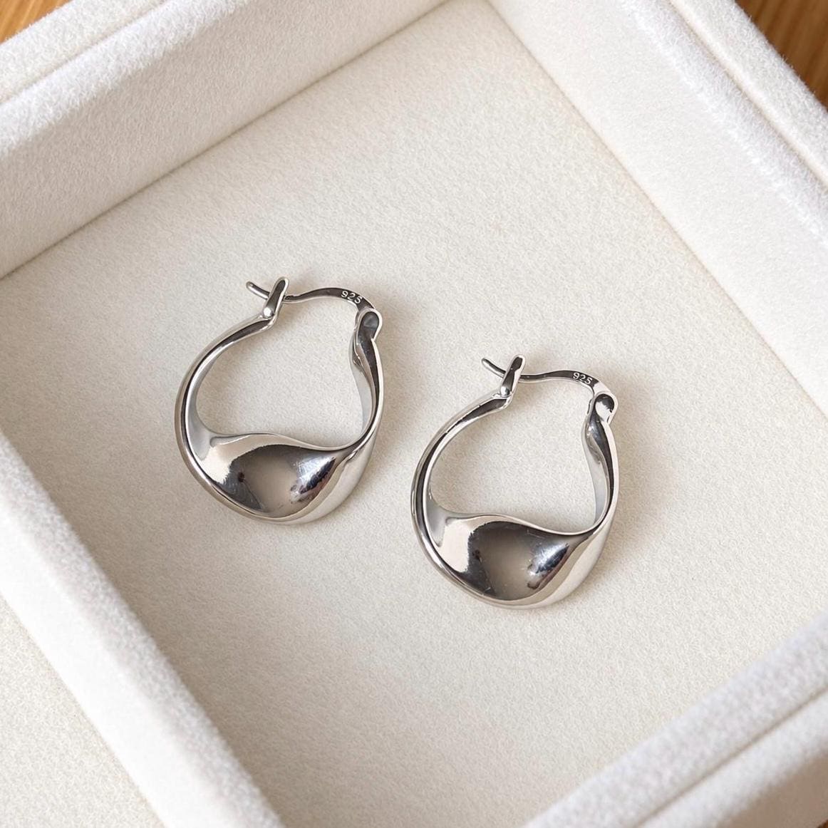 Pair of sterling silver twisted teardrop hoop earrings laid flat in velvet box