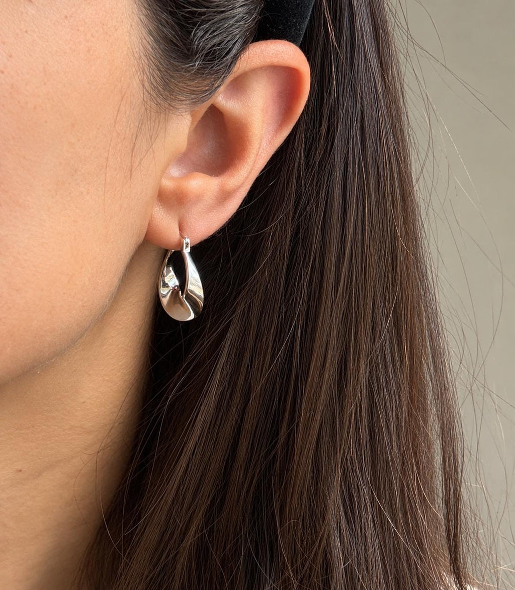 Model wearing polished sterling silver sculptural teardrop hoop earring