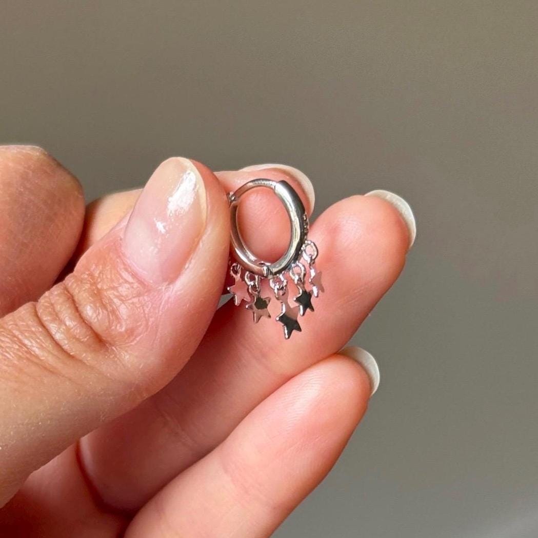 Close-up of sterling silver star charm hoop earring held between fingers