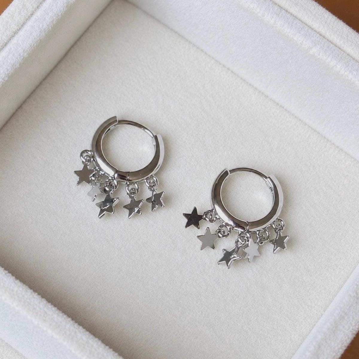 Pair of polished sterling silver star charm huggie hoops on ivory velvet