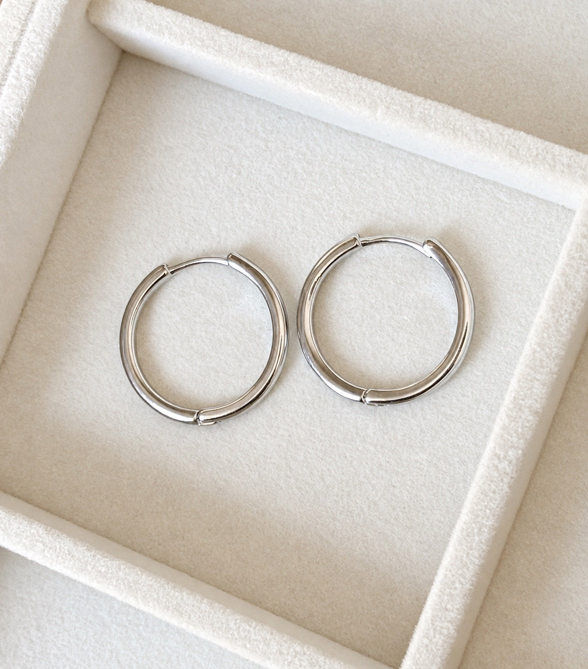 Pair of polished 925 sterling silver hoop earrings displayed on cream velvet
