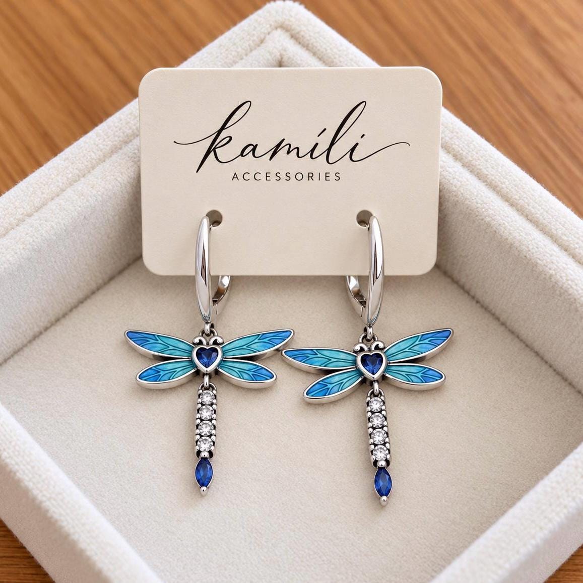 Pair of blue enamel dragonfly earrings displayed on Kamíli Accessories branded card