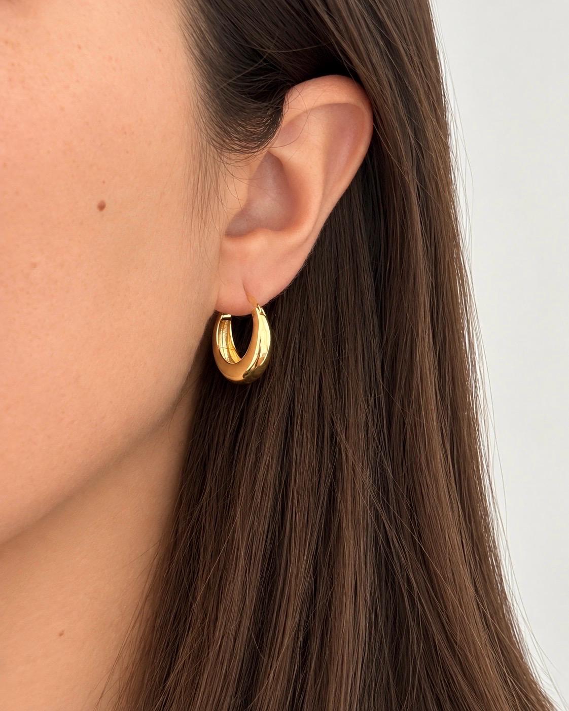 Gold-finish chunky crescent hoop earring worn on an ear