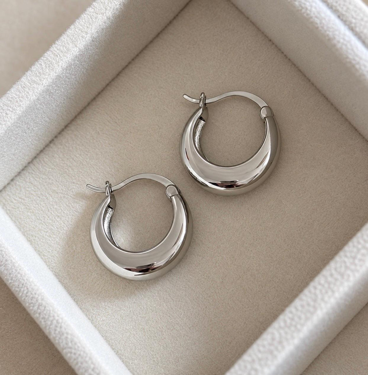 Silver-finish crescent hoop earrings on a jewellery tray