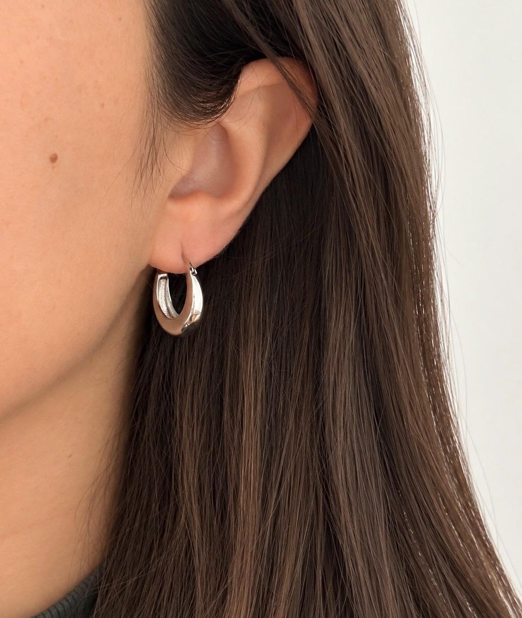 Silver chunky crescent hoop earring worn on an ear