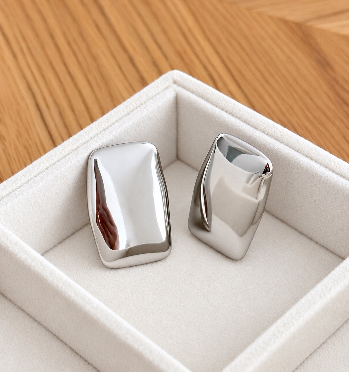 Two sculptural silver-tone stainless steel rectangular stud earrings displayed upright in velvet tray