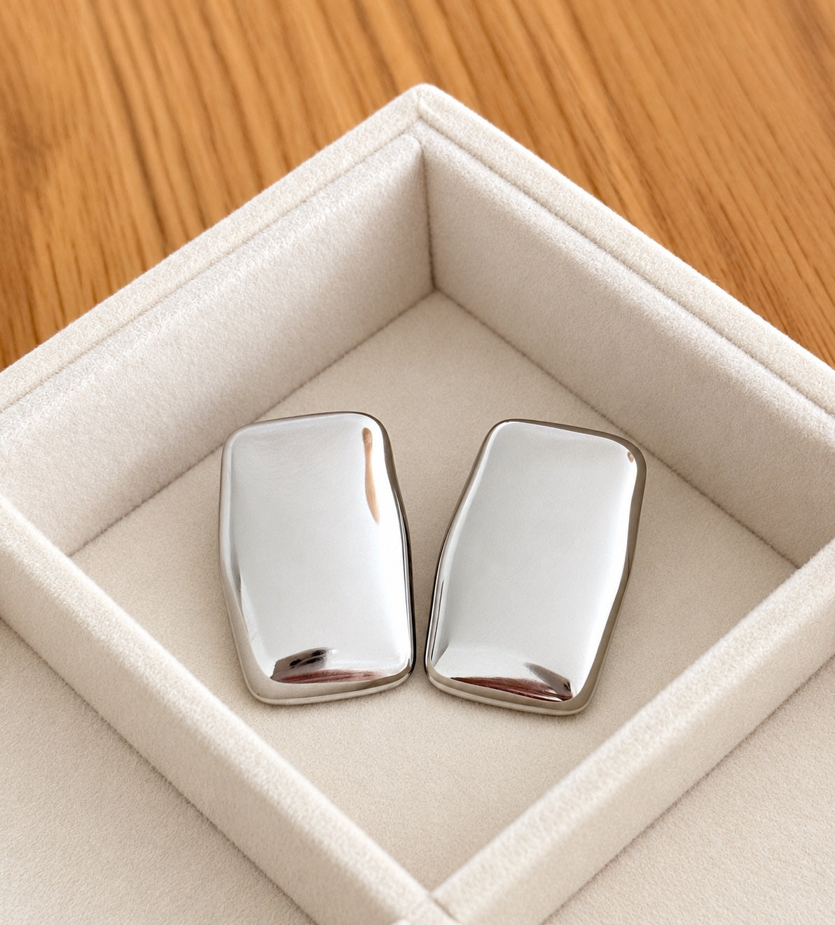 Pair of chunky polished silver rectangular stud earrings resting in an ivory velvet jewellery tray