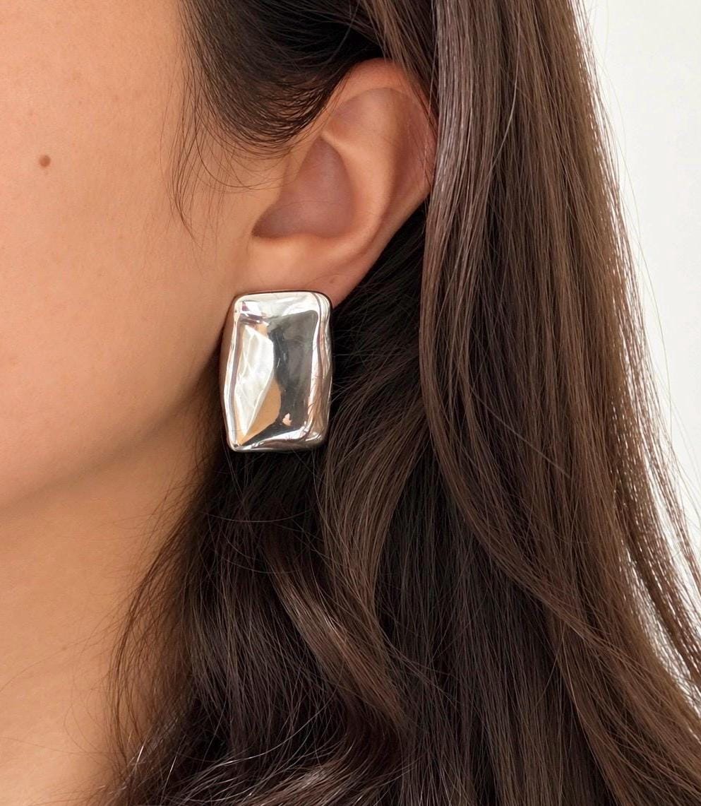 Chunky mirror-finish silver rectangular stud earring worn on the ear showing its statement size