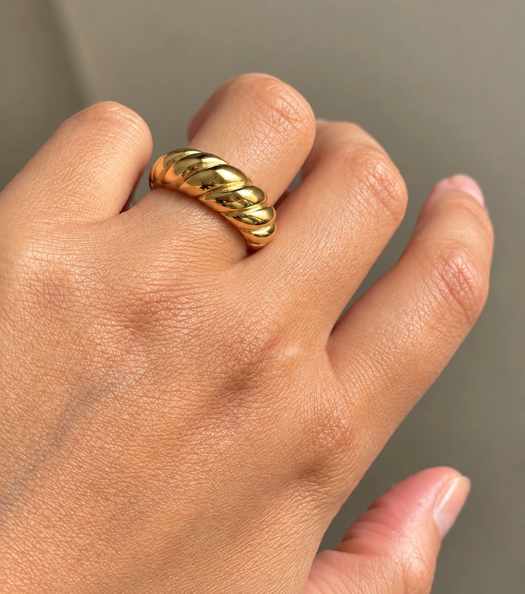 Close-up of shiny gold plated twisted croissant statement band on finger