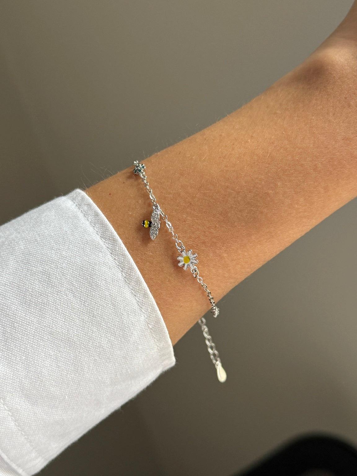 Silver nature-inspired bracelet with bee and daisies worn on wrist