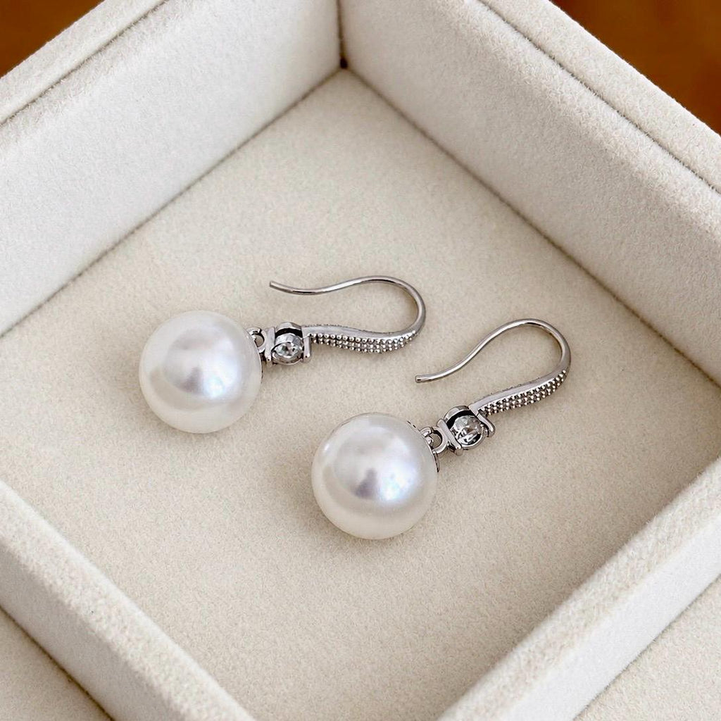 White pearl dangling earrings with curved silver ear hooks displayed on cream velvet
