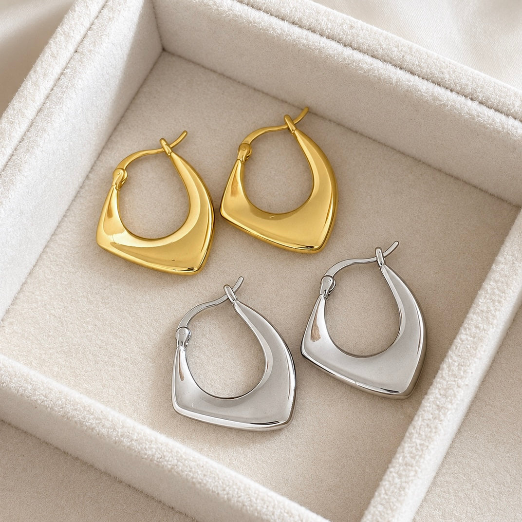 Gold and silver finishes of geometric hoop earrings photographed together on cream display