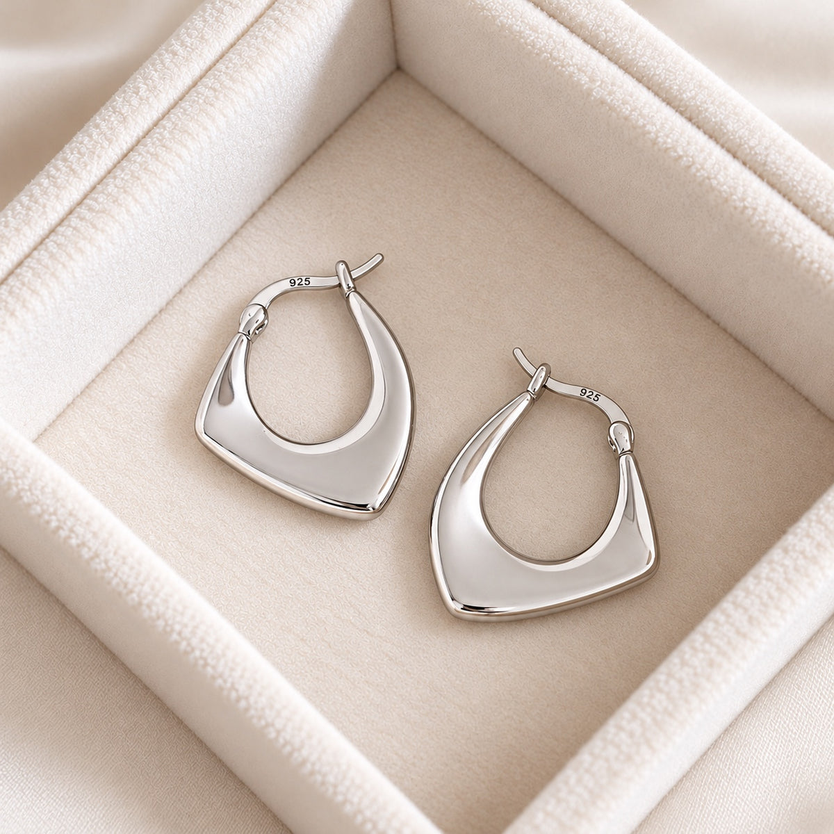 Silver colour 925 sterling silver geometric hoop earrings on cream jewellery tray