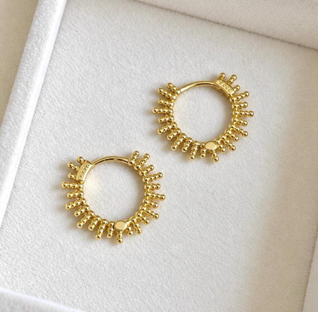 Pair of gold plated sterling silver beaded sunburst hoop earrings laid on soft ivory velvet