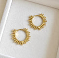 Pair of gold plated sterling silver beaded sunburst hoop earrings laid on soft ivory velvet