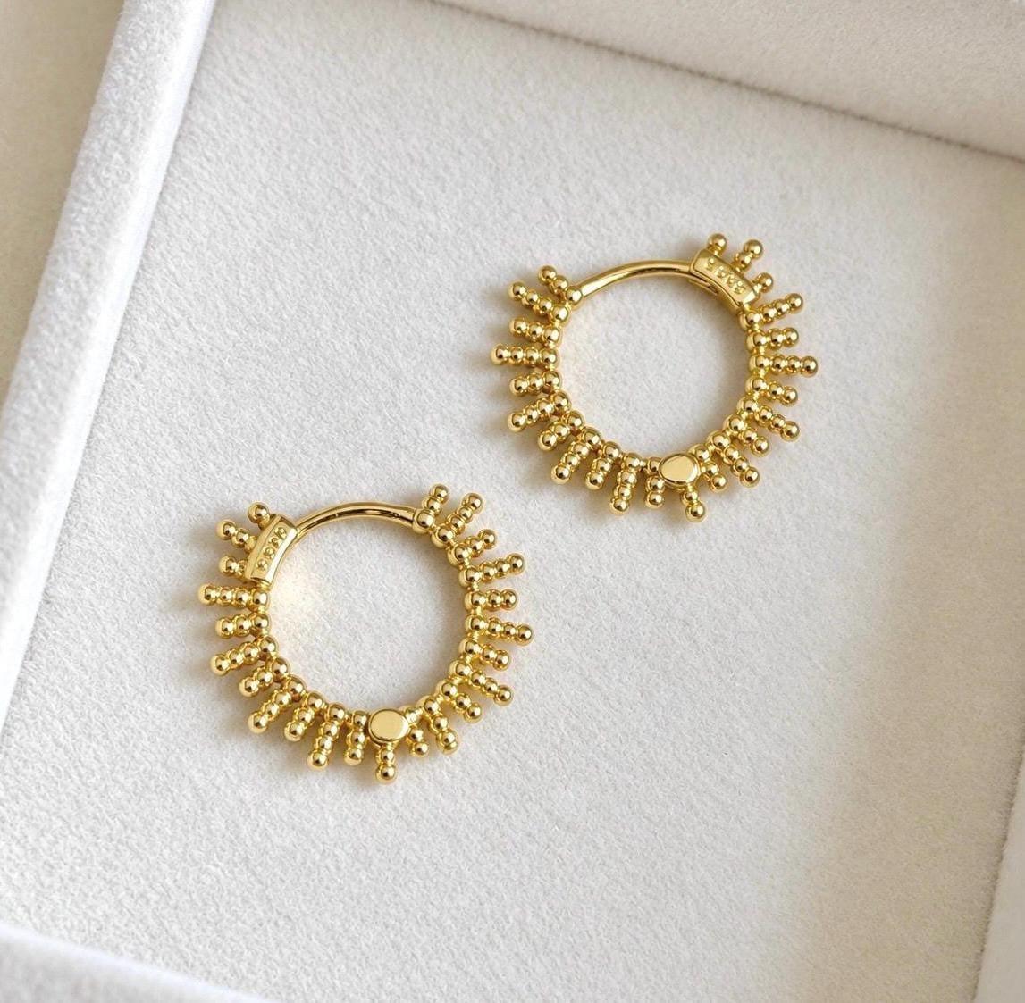 Pair of gold plated sterling silver beaded sunburst hoop earrings laid on soft ivory velvet