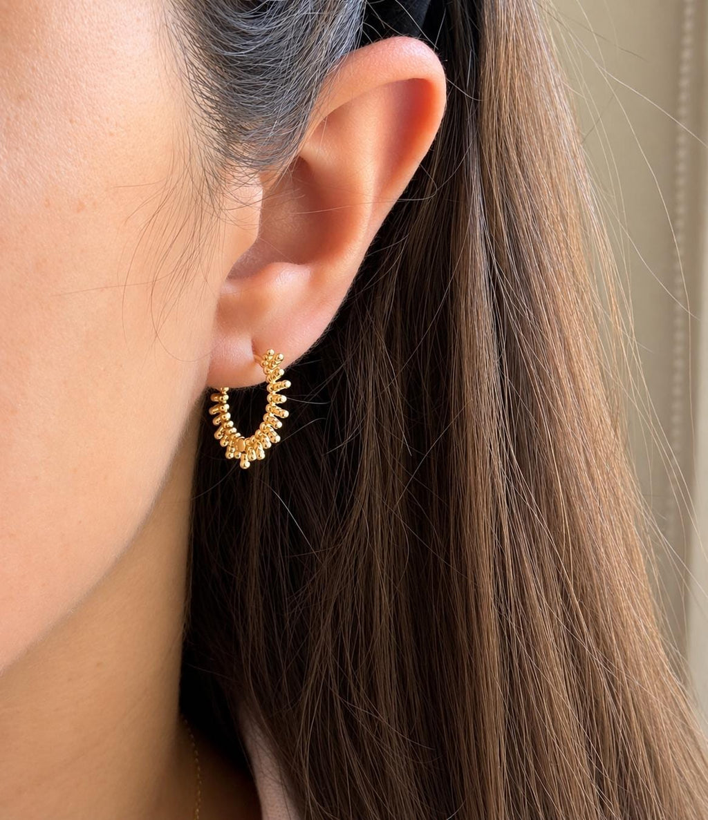 Gold beaded sunburst hoop earring modelled on ear