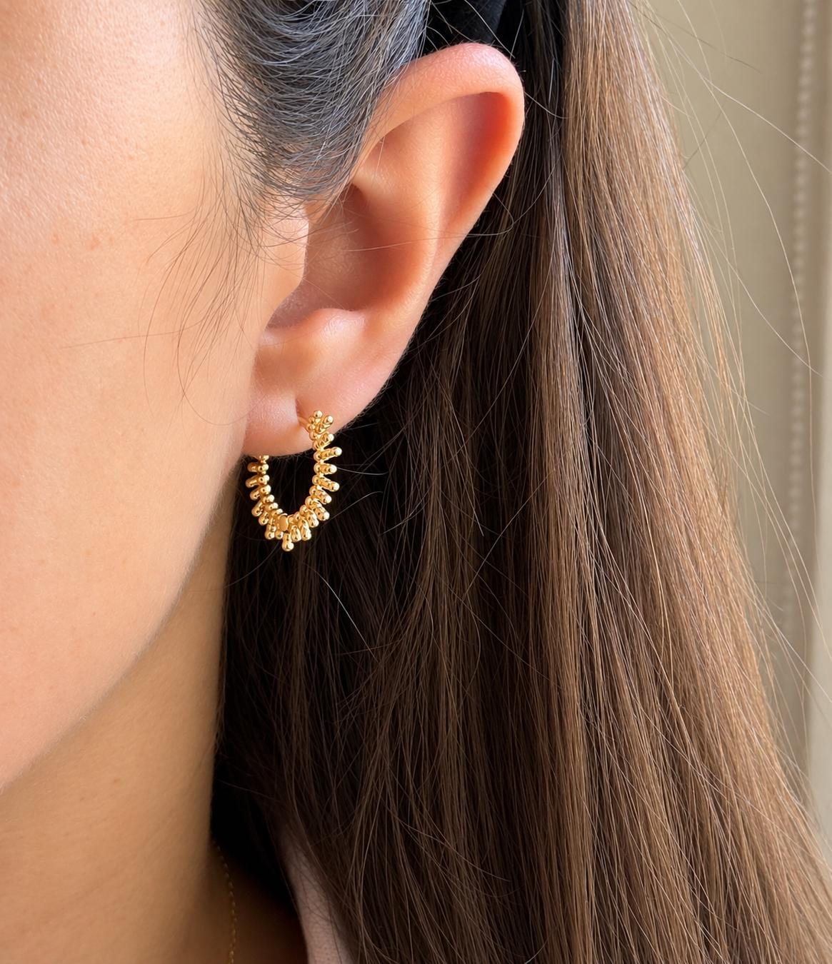 Gold beaded sunburst hoop earring modelled on ear