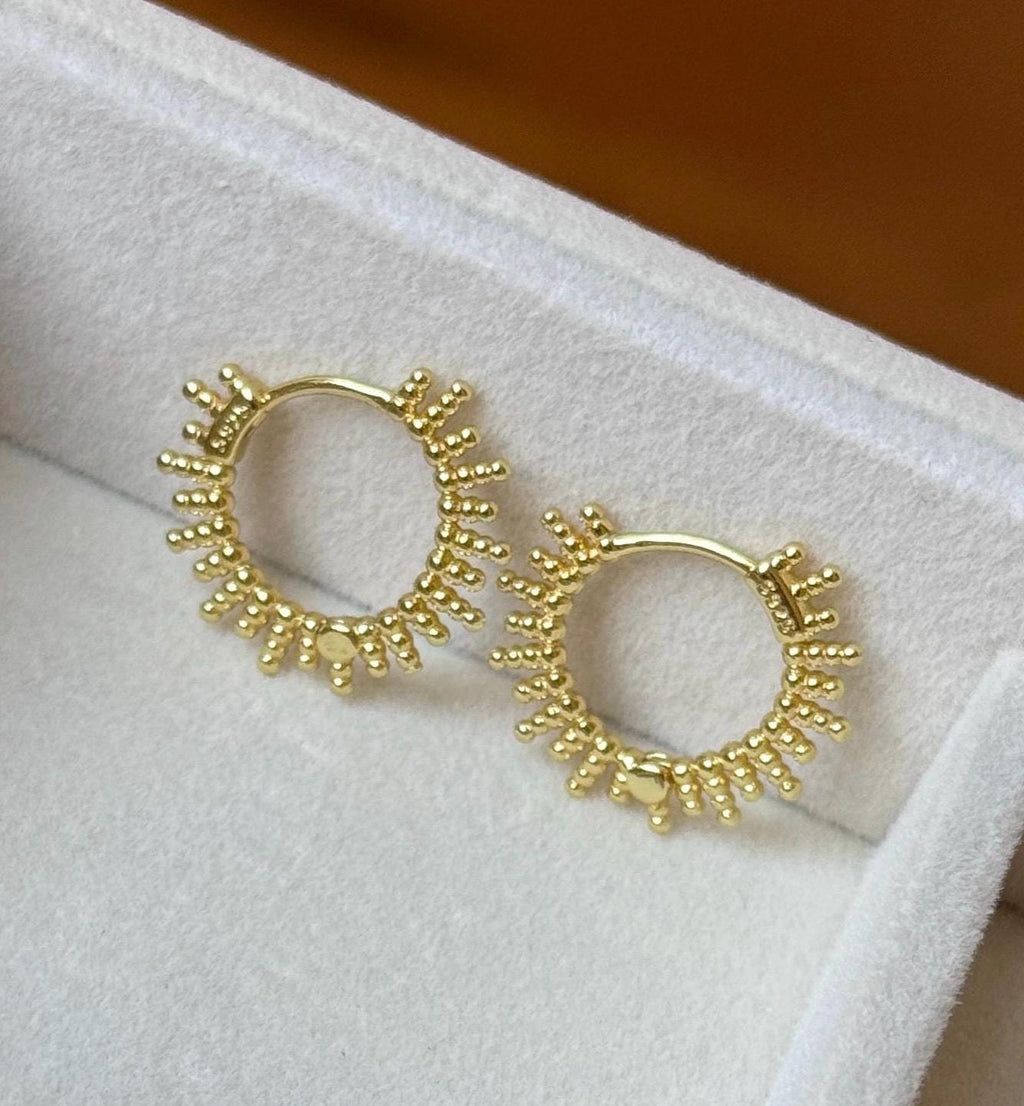 Two gold beaded celestial sunburst hoops shown from front on a velvet jewellery cushion