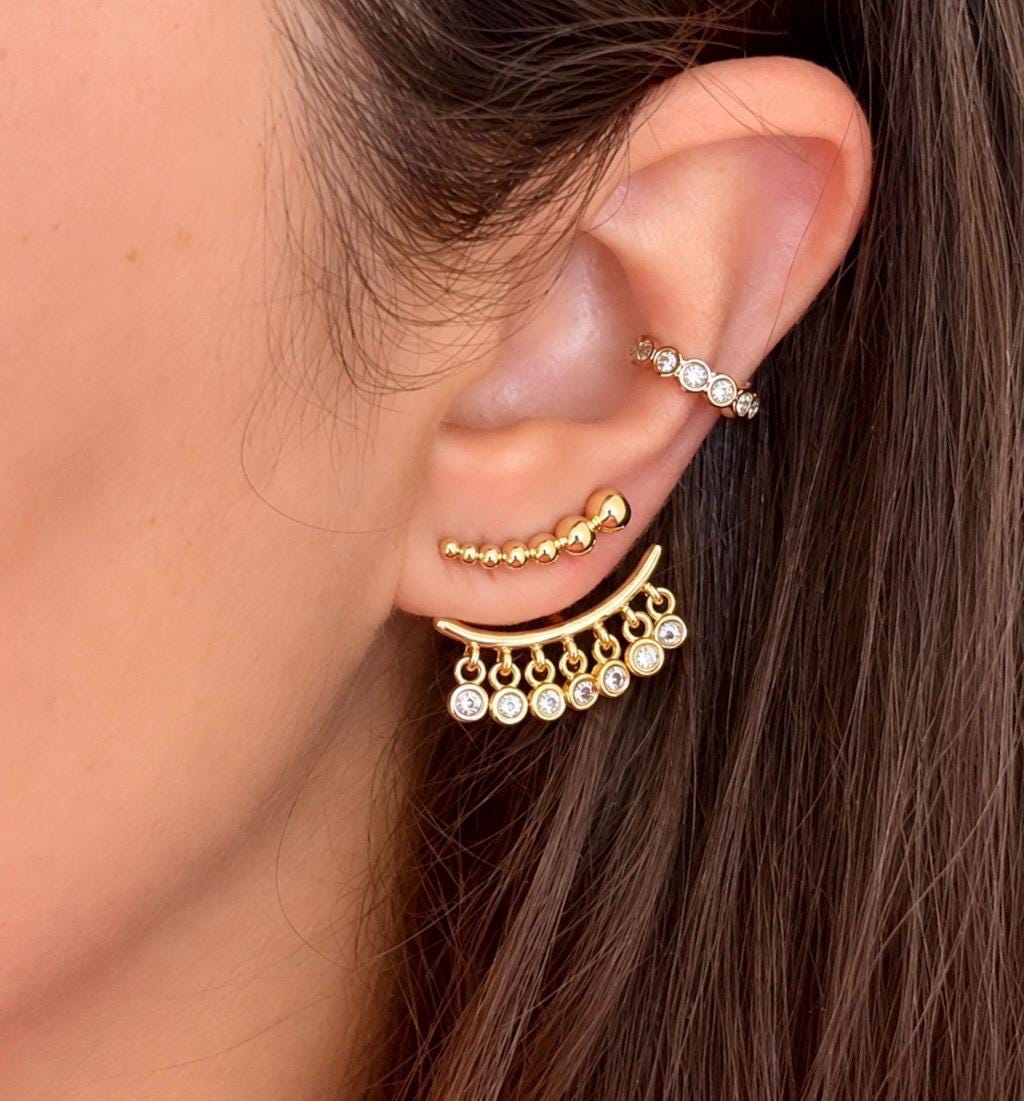 Gold plated ear jacket earrings worn, featuring graduated gold beads and dangling clear cubic zirconia stones