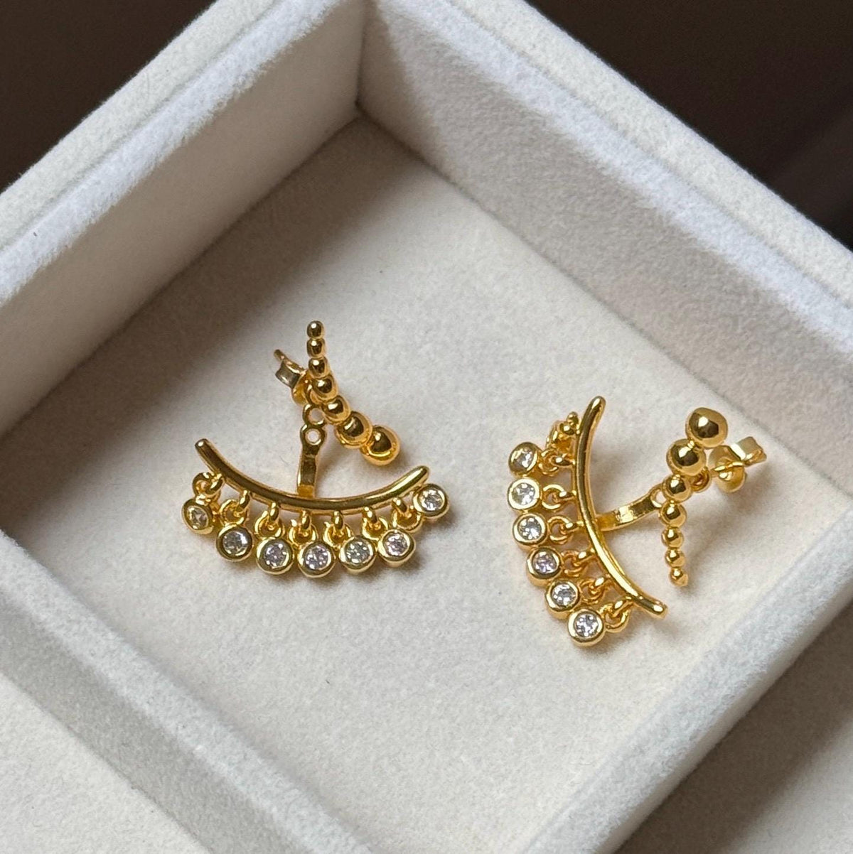 Gold ear jacket earrings displayed on velvet showing curved bars, graduated beads and clear CZ dangles