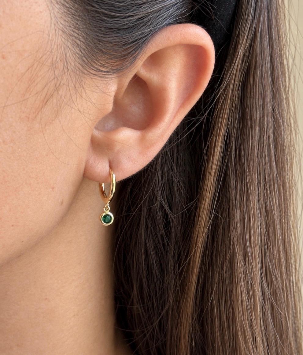 Gold colour huggie hoop earring with green cubic zirconia drop worn on ear