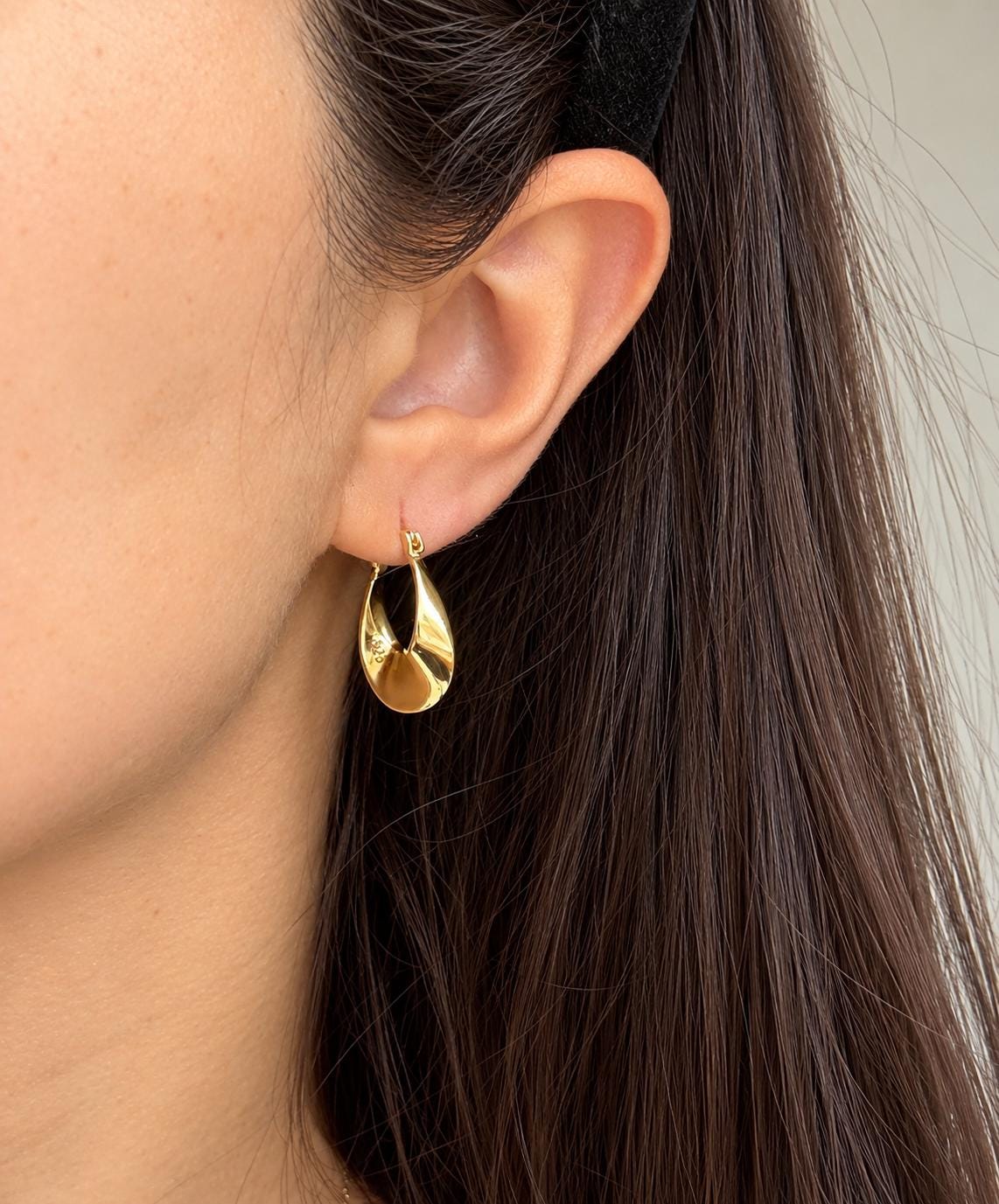 Gold plated sterling silver sculptural twisted teardrop hoop earring worn on the ear