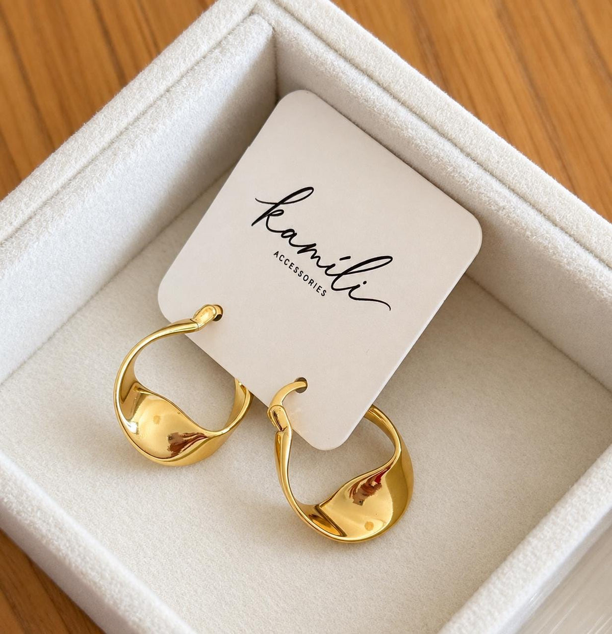 Gold plated twisted hoop earrings on Kamíli Accessories card inside cream jewellery tray