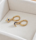Gold plated sterling silver mismatched blue cubic zirconia crescent moon and star huggie earrings on ivory velvet
