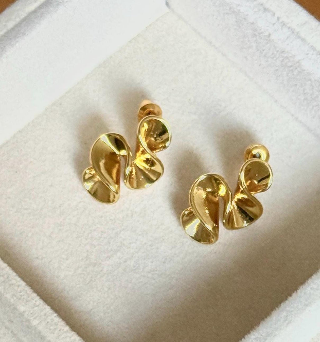 Close up of gold-plated flowing abstract swirl stud earrings on cream velvet