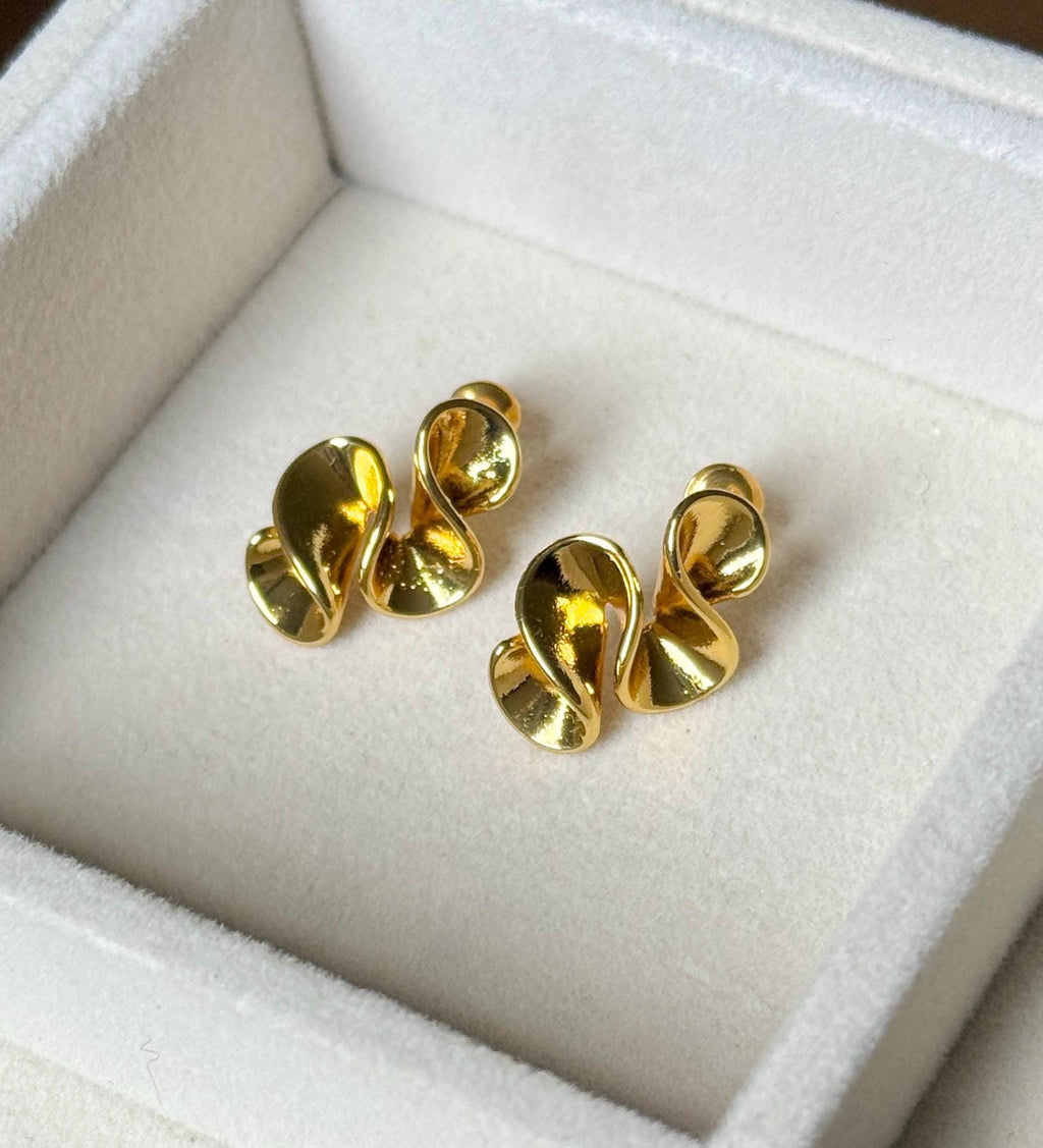 Pair of polished gold-tone folded ribbon sculptural stud earrings on cream velvet