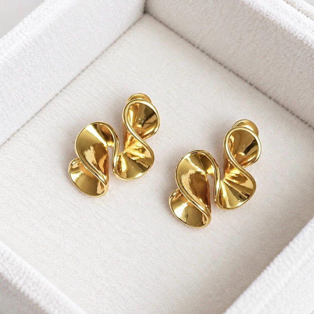 Pair of polished gold-tone abstract sculptural swirl stud earrings on soft cream velvet