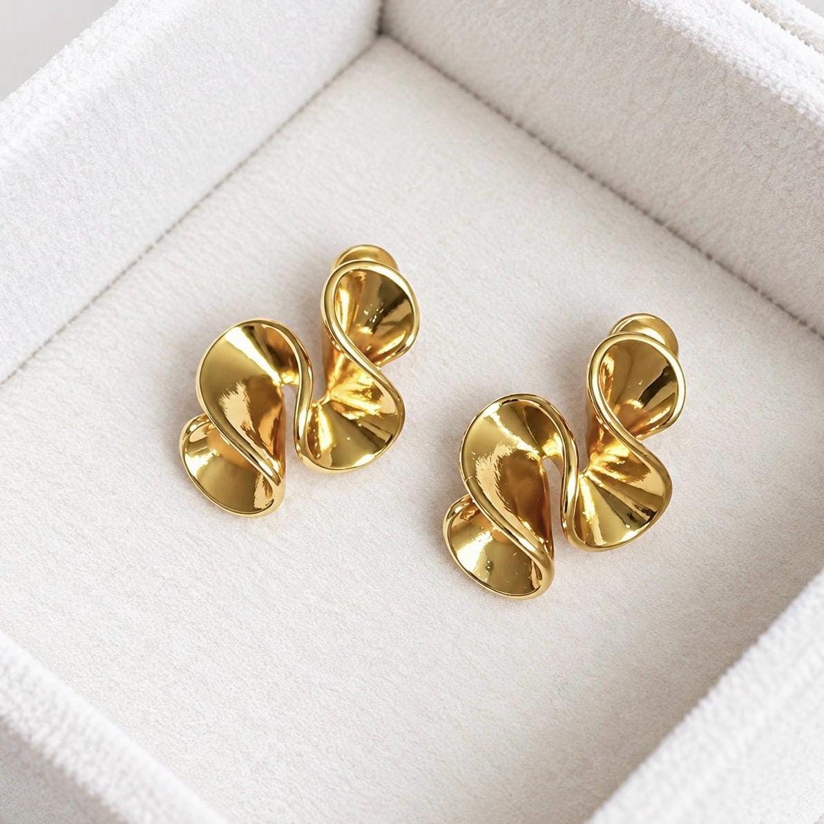 Pair of polished gold-tone abstract sculptural swirl stud earrings on soft cream velvet