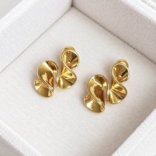 Pair of polished gold-tone abstract sculptural swirl stud earrings on soft cream velvet