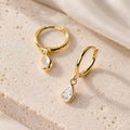 Gold-plated sterling silver huggie hoop earrings with clear teardrop CZ charms on cream stone