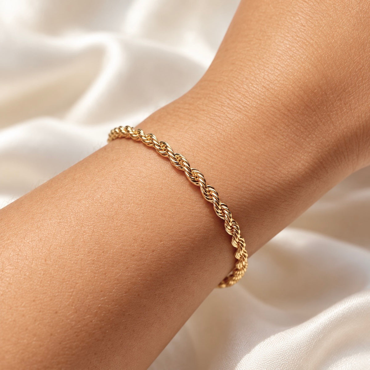 Polished gold twisted rope bracelet shown on wrist against light fabric